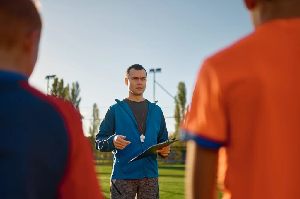 Young soccer coach teaching kids on football field