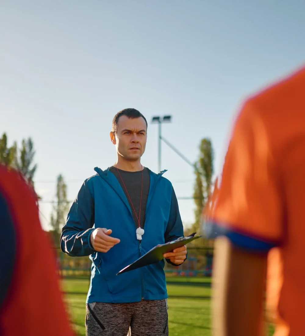 Young soccer coach teaching kids on football field